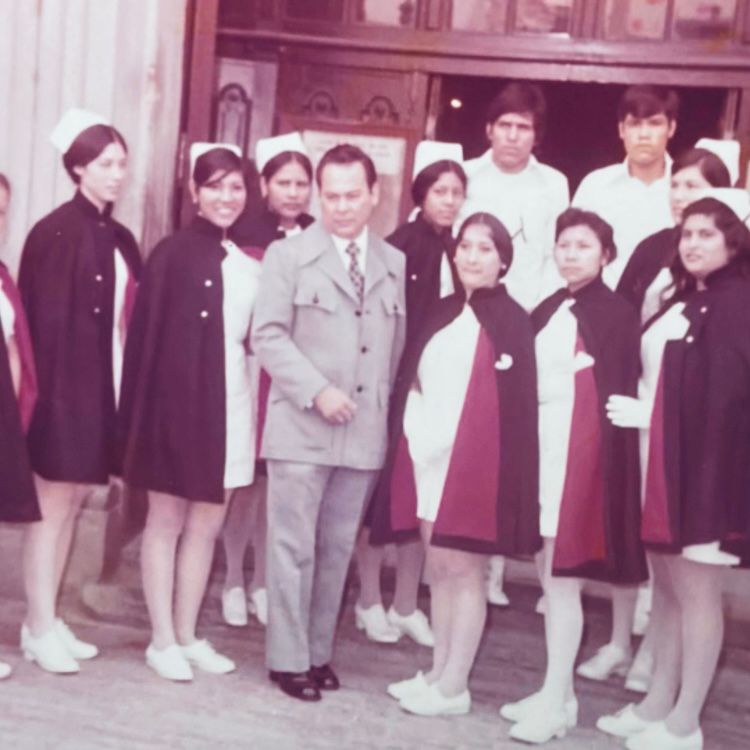 Fotografía antigua de un grupo de alumnas de Enfermería con capa y uniforme, junto a un hombre de traje