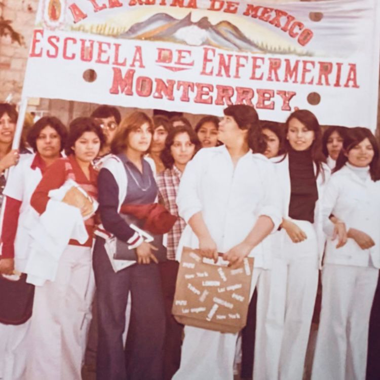 Fotografía antigua de alumnas de Enfermería reunidas bajo una manta con el nombre de la escuela