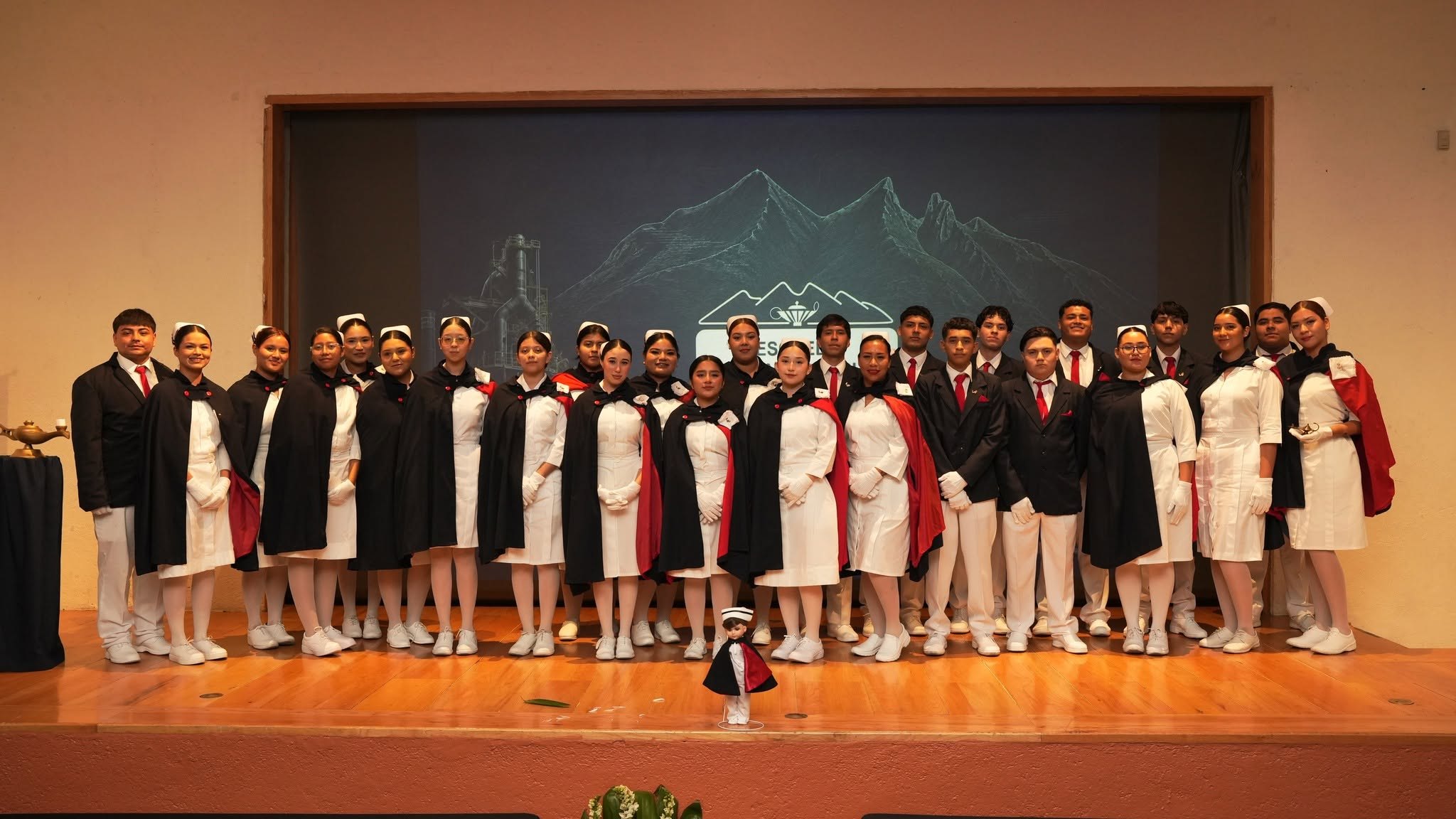 Grupo de alumnos de Enfermería con capa, cofia y traje, reunidos en el escenario durante la ceremonia