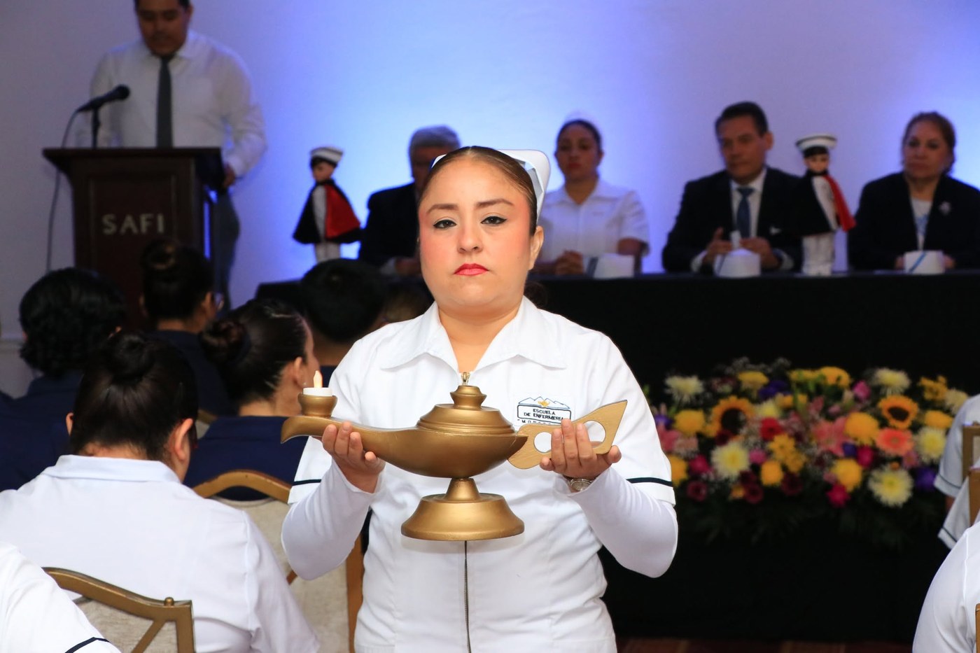 Una alumna de Enfermería con cofia sostiene la lámpara tradicional durante la ceremonia