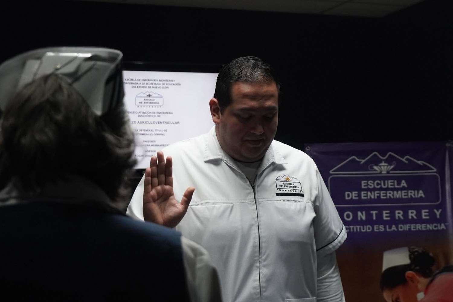 Un alumno de Enfermería con uniforme blanco levanta la mano durante el juramento