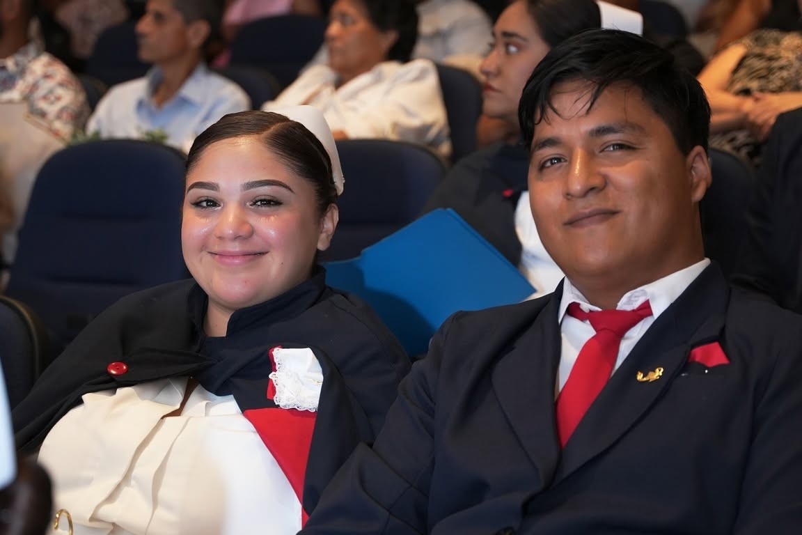 Una alumna y un alumno de Enfermería con uniforme de gala, sonrientes durante la ceremonia